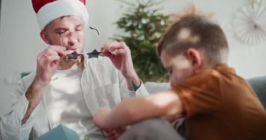Bir baba Noel Baba şapkası takar ve yıldız şeklinde gözlük takar, oğlunu maskaralıklarla eğlendirir ve eğlenceli Noel anıları yaratır..