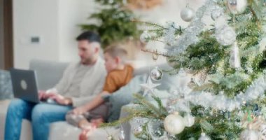 Genç bir çocuk Noel boyunca babasının dizüstü bilgisayarda çalışmasını izliyor. Oturma odasında sakin ve rahat bir anı paylaşıyorlar..