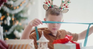 Genç bir çocuk Noel hediyelerini neşeyle paketliyor, dikkatle kurdeleleri bağlıyor ve neşeli hediyeler hazırlıyor, ailesiyle sıcak ve neşeli bir tatil ortamı yaratıyor..