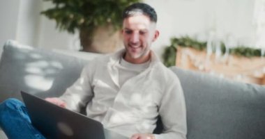 Gülümseyen genç bir iş adamı, ev bilgisayarında uzaktan çalışmaktan keyif alır. İşlerini verimli ve rahat bir şekilde yürütür..