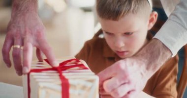 Genç bir çocuk, babasının Noel hediyesini paketlemesine hevesle yardım eder. Birlikte bayram hediyesi hazırlamak için kurdele ve kağıtları dikkatle taşır..