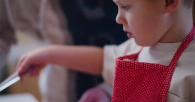 Genç bir çocuk çiğ yumurtayı dikkatlice kurabiyelerin üzerine yayar, onları pişirmeye ve altın bir son için hazırlar..