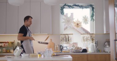 Bir adam mutfakta yemek pişirirken tavada ustaca krep çevirir..