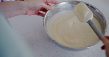 Bir kadın krep hamuru yoğunluğunu kontrol etmek için plastik spatula kullanır..