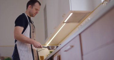 Bir adam mutfakta yemek pişirirken tavada krep çeviriyor..