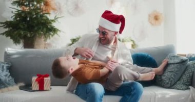 Noel Baba şapkalı bir baba Noel 'de oğlunu koltukta gıdıklıyor. Birlikte gülüp eğleniyorlar..