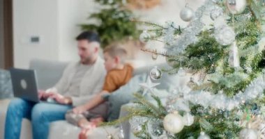 Genç bir çocuk Noel boyunca babasının dizüstü bilgisayarda çalışmasını izliyor. Oturma odasında sakin ve rahat bir anı paylaşıyorlar..