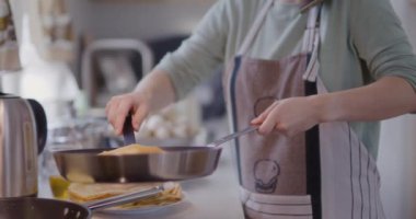 Bir kadın mutfakta yemek pişirirken tavada krep çevirir..