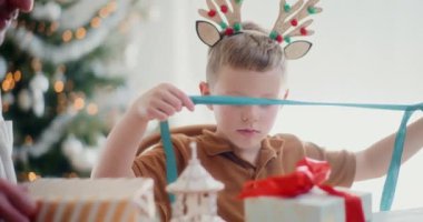 Genç bir çocuk Noel hediyelerini neşeyle paketliyor, dikkatle kurdeleleri bağlıyor ve neşeli hediyeler hazırlıyor, ailesiyle sıcak ve neşeli bir tatil ortamı yaratıyor..