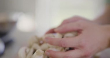 Kesilmiş mantarları mutfaktaki bir kaseye aktaran ellerin detaylı görüntüsü..