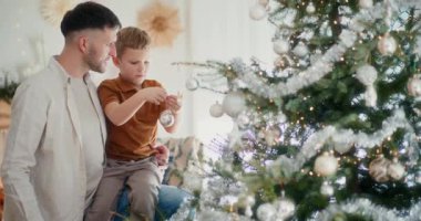 Bir baba ve çocuğu Noel ağacına güzel mücevherler asar, neşeli bir anı paylaşırlar.
