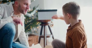 Bir baba ve oğlu ağaçlara renkli bir Noel mücevheri asar ve birlikte neşeli anılar yaratırlar..