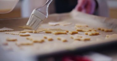 Çiğ yumurtanın kurabiyelerin üzerine serpilmesi, pişirmeden önceki son hazırlık adımını gösteriyor..
