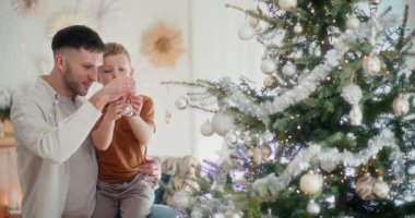 Genç bir çocuk ve babasının Noel ağacına dikkatlice mücevher yerleştirdikleri yakın plan bir fotoğraf.