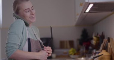 Mutfakta yemek pişiren ve telefonda konuşan mutlu bir kadın..