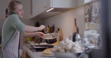 Bir kadın mutfakta telefonla konuşurken yemek hazırlar..