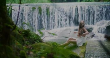 Güzel bir kadın şelalenin önünde dinlenir ve meditasyon yapar, doğada huzur, denge ve ilham bulur..