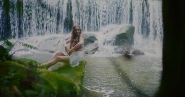 Güzel bir kadının sakin portresi şelalenin önünde huzur içinde dinleniyor. Etrafı yemyeşil..