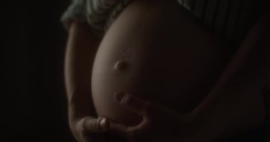 Hamile bir kadının hassas bir şekilde ellerini karnına koyduğu yakın çekim..