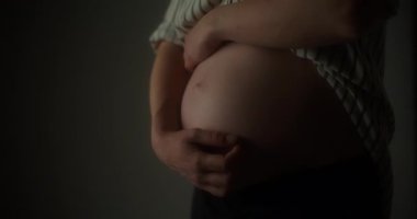 Hamile bir kadının hassas bir şekilde ellerini karnına koyduğu yakın çekim..