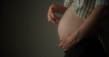 Hamile bir kadın karnını nazikçe okşar, doğmamış çocuğuyla sevgi ve bağını gösterir..