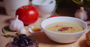 Kremalı beyaz sebze çorbası. Arka planda renkli çiğ sebzelerle servis ediliyor..