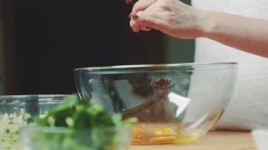 Bir kadın yumurtaya biber katar, baharat katar ve pişirme hazırlığı için karıştırır..