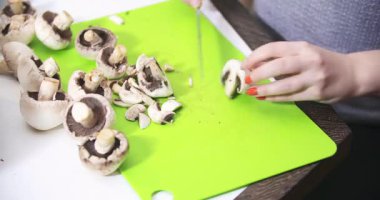 Bir kadın, zengin mantar sosu hazırlığının bir parçası olarak taze mantarları dörde böler ve mutfakta dikkatle çalışır..