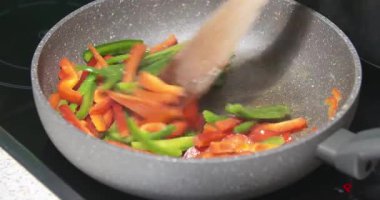 Bir tavada beyazlayan sarı, yeşil ve kırmızı biberlerin yakın çekimi.