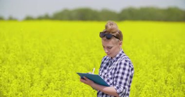 Çiçek açan bir kolza tohumu tarlasında duran mutlu genç bir kadın çiftçinin portresi. Modern tarım ve kırsal yaşam tarzı kavramı.