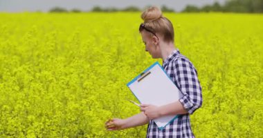 Tarım alanında kolza bitkilerinin kalitesini ve büyümesini kontrol eden dişi çiftçi. Ekin sağlığı izleme ve bitki geliştirme kavramı.