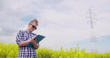 Kolza tohumu tarlasının yanında duran bir kadın çiftçi not defterine not alıyor. Ekin izleme, veri toplama ve sürdürülebilir tarım kavramı.