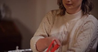Genç bir kadın Noel hediyelerini dekoratif kurdeleler ve kağıtlarla bir masaya sarar..
