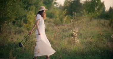 Elinde kamera tutan bir kız otlak bir çayırda doğanın huzurlu güzelliğinin tadını çıkarıyor.