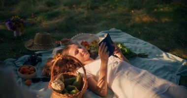 Sakin bir kız, sıcak yaz güneşinin altında çayırda güneşlenirken battaniyeye uzanır.