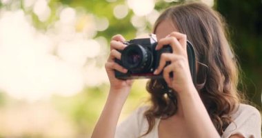 Genç bir kız dışarıda doğal ışık altında retro film kamerasıyla fotoğraf çekiyor.