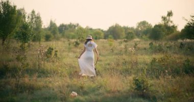 Genç, gülümseyen bir fotoğrafçı kamerasını doğayla çevrili sıcak güneş ışığında tutuyor.