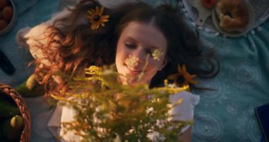 Hayalperest bir genç kız doğada çimenler ve güneş ışığı altında huzur içinde yatıyor.