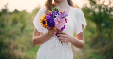 Gün batımında genç bir kızın elinde renkli bir çiçek buketinin yakın çekimi.