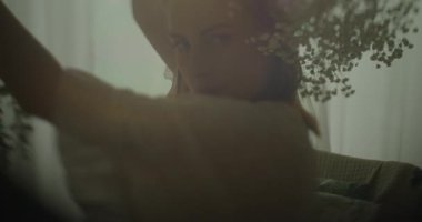 Hamile bir kadın, şehvetli bir fotoğraf çekimi sırasında elinde bir buket bebek nefesi tutarak, nostaljik ve duygusal bir görünüm sergiliyor..