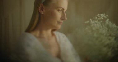 Düşünceli bir kadın pencereden dışarı bakar, nostalji ve hayallerle yansıtır, elinde bir buket çıngıraklı yılanla.