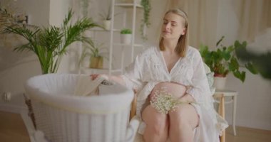 Huzurlu hamile bir kadın beşiği nazikçe sallıyor, neşeli ve hayalperest görünüyor..