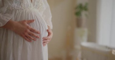 Hamile bir kadının elleri nazikçe karnını okşar, beklenti ve annelik sevgisini iletir..