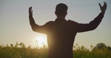 Mutlu bir çiftçinin silueti kanola tarlasında günbatımının tadını çıkarıyor, tarımın ve doğanın güzelliğini yakalıyor..