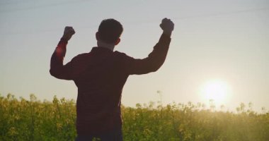 Neşeli bir çiftçi elleri havada, kolza tohumu açarken başarıyı kutluyor. Görünüşte mutlu ve memnun..