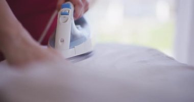 Bir kadının ev ortamında ütü masasında giysileri ütülemesinin detaylı görüntüsü..