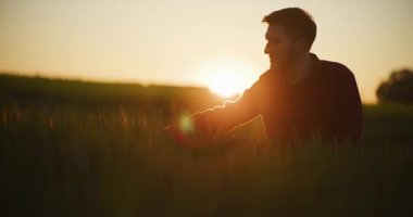 Bir çiftçi gün batımında altın buğday saplarına nazikçe dokunur manzaralı bir tarım tarlasında, hasat zamanını ön plana çıkarır..