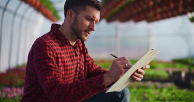 Profesyonel bir bahçıvan fabrikaları teftiş ederken bir serada notlar alır, bitki koşullarını analiz eder..
