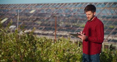 Arka planda sera ve tüm bahçecilik çiftliği olan defterine notlar yazan bir çiftçinin yakın plan görüntüsü..