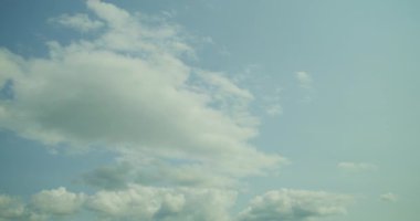 Pofuduk beyaz bulutların zamanı parlak mavi gökyüzünde ilerlerken güneşli bir günün güzelliğini yakalıyor..